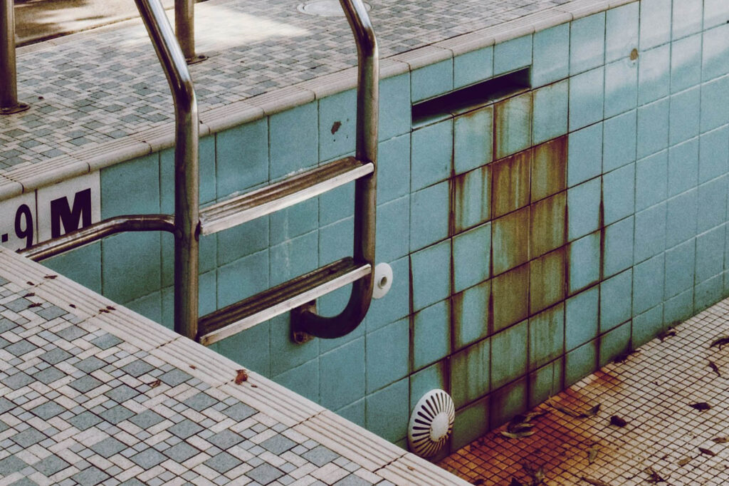 Pool stains and metal corrosion on tile walls near ladder creating potential health and safety risks