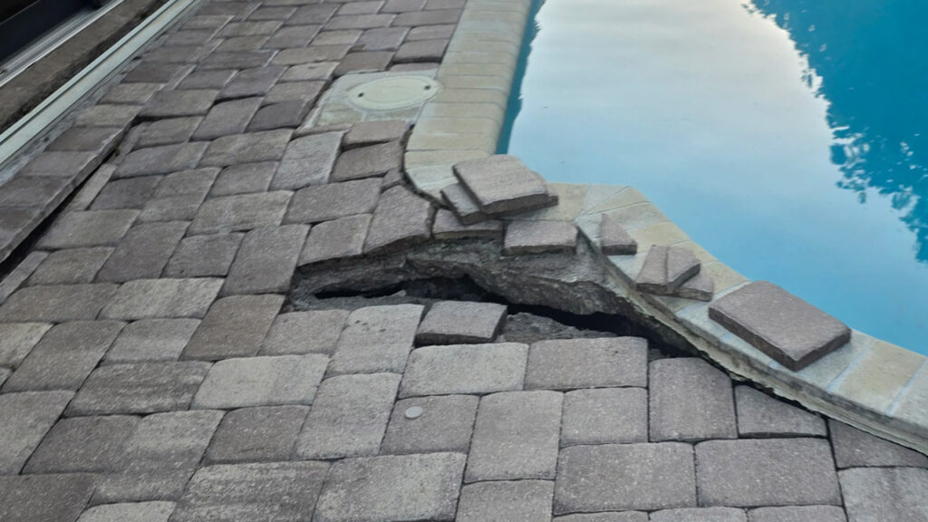 Sunken pavers and exposed ground near a pool deck caused by underground water leakage.